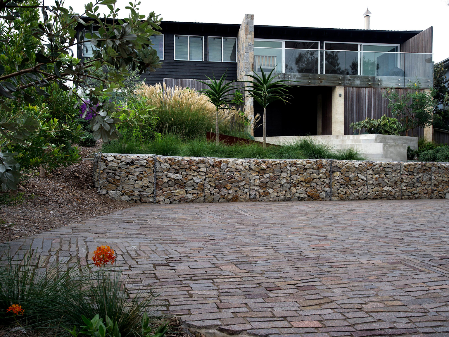 Porphyry filetti driveway, stone gabion wall in front of organic style beach house