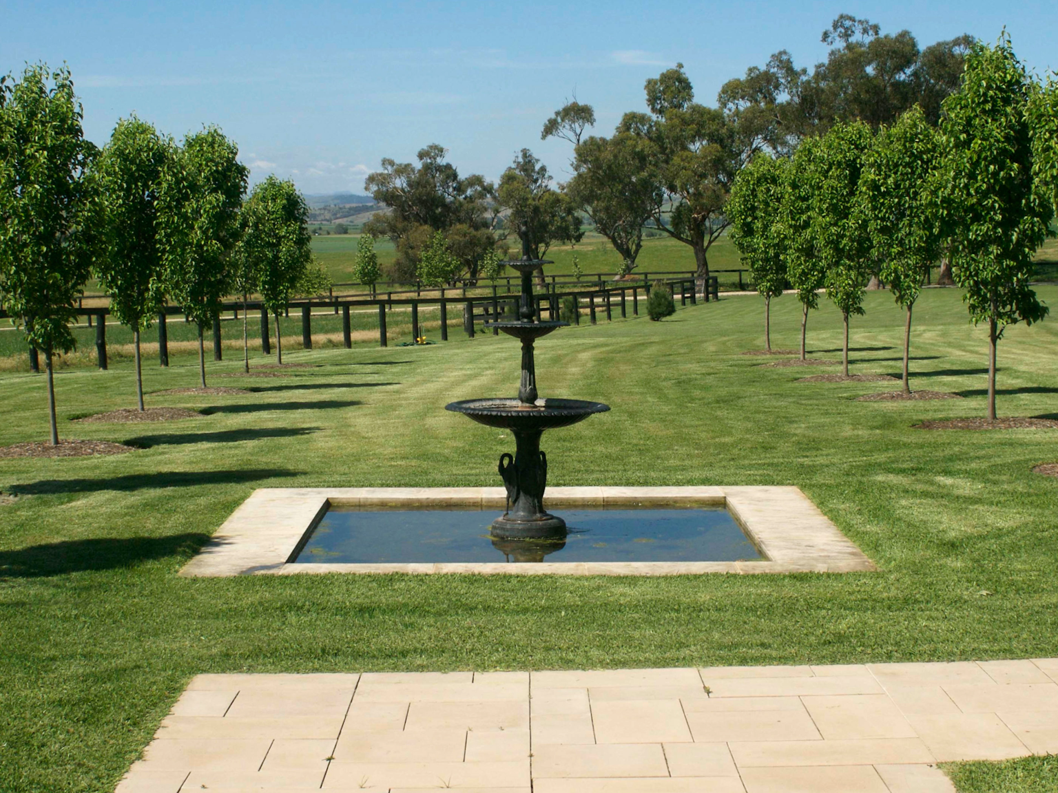 Pond fountain beside pathway using Hawkesbury concrete pavers with avenue of trees behind