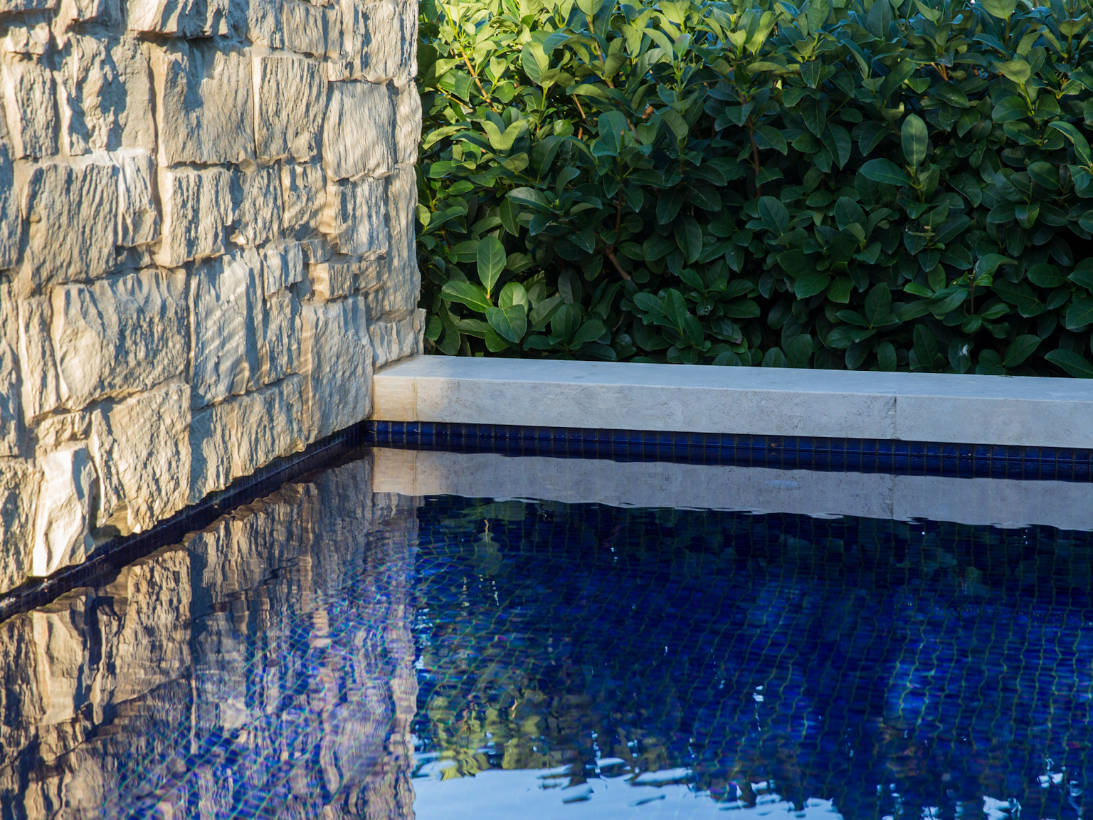 Scala travertine rebated coping units around pool with Newport limestone feature wall